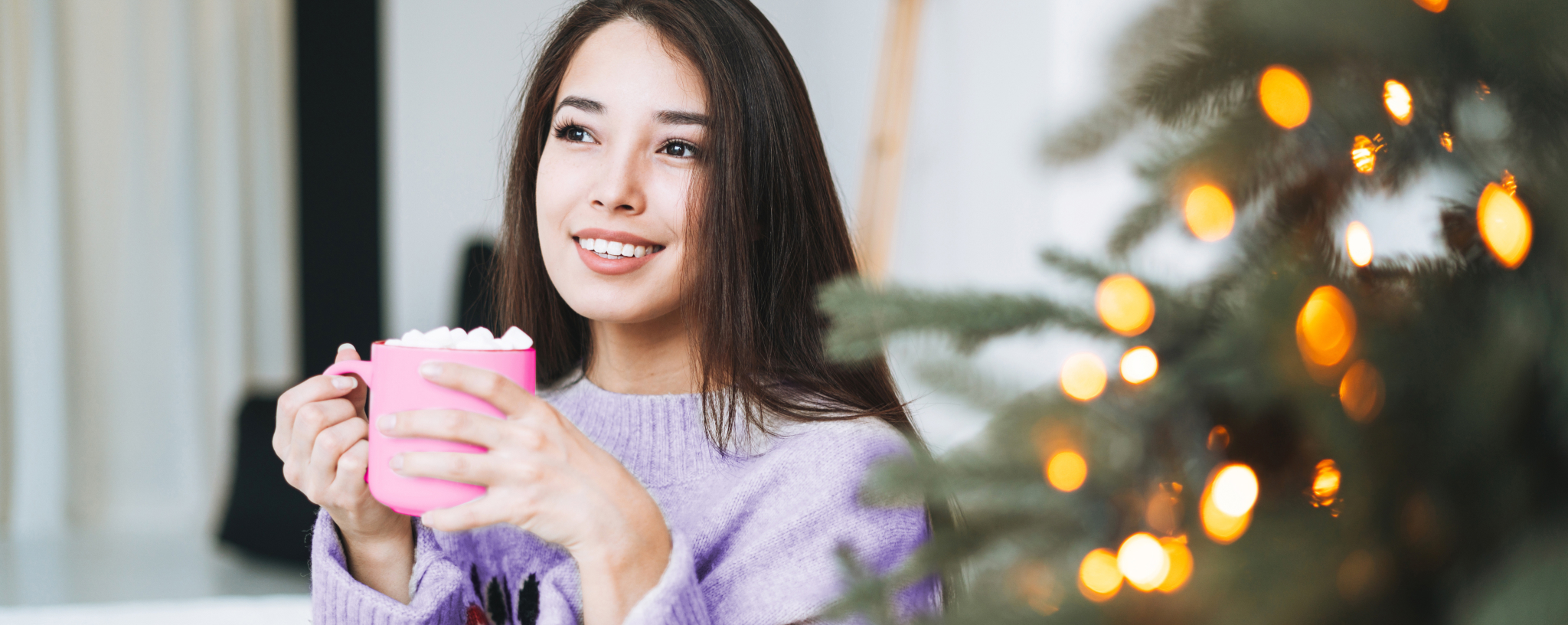 Lady drinking a hot chocolate next to a Christmas tree