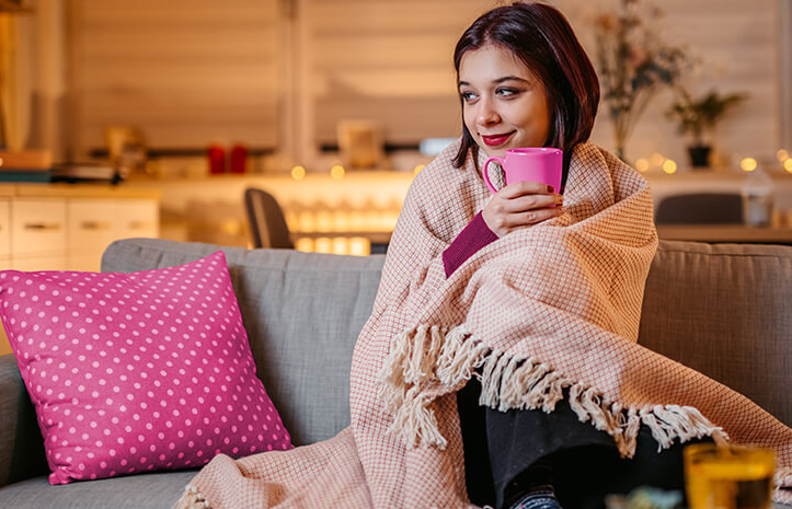 Lady snuggled under a blanket drinking a warm drink from a mug