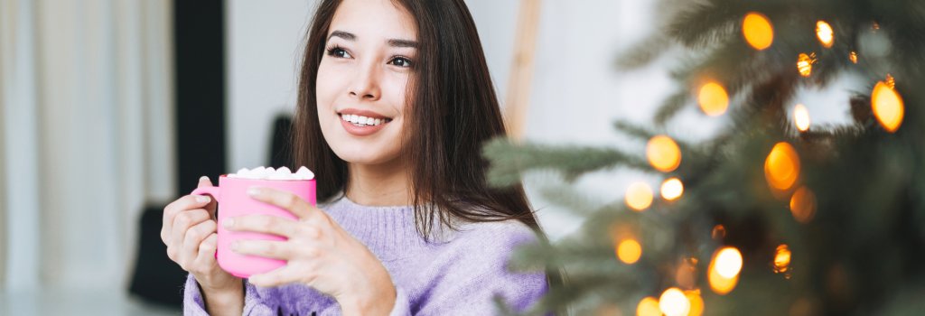 Lady drinking a hot chocolate next to a Christmas tree